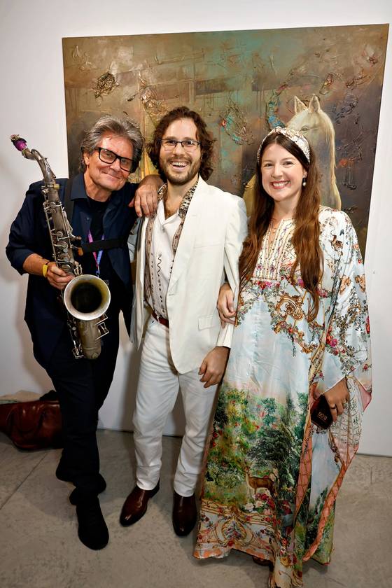 Scott Page holding a saxophone, standing with Vaughn Bergen and Kayla Rose Bergen in front of a large painting at ACA Galleries.