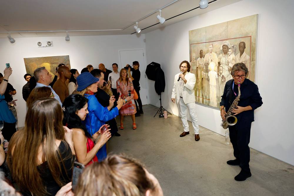 Vaughn Bergen singing into a microphone beside Scott Page playing saxophone, in a gallery room at ACA Galleries, with a crowd holding phones up and a large figurative painting on the wall behind them.