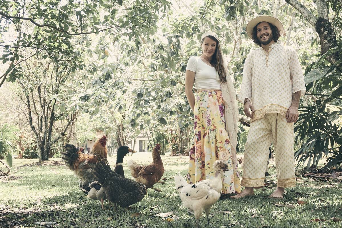 Kayla and Vaughn standing barefoot under fruit trees, chickens and a duck on the grass around them.