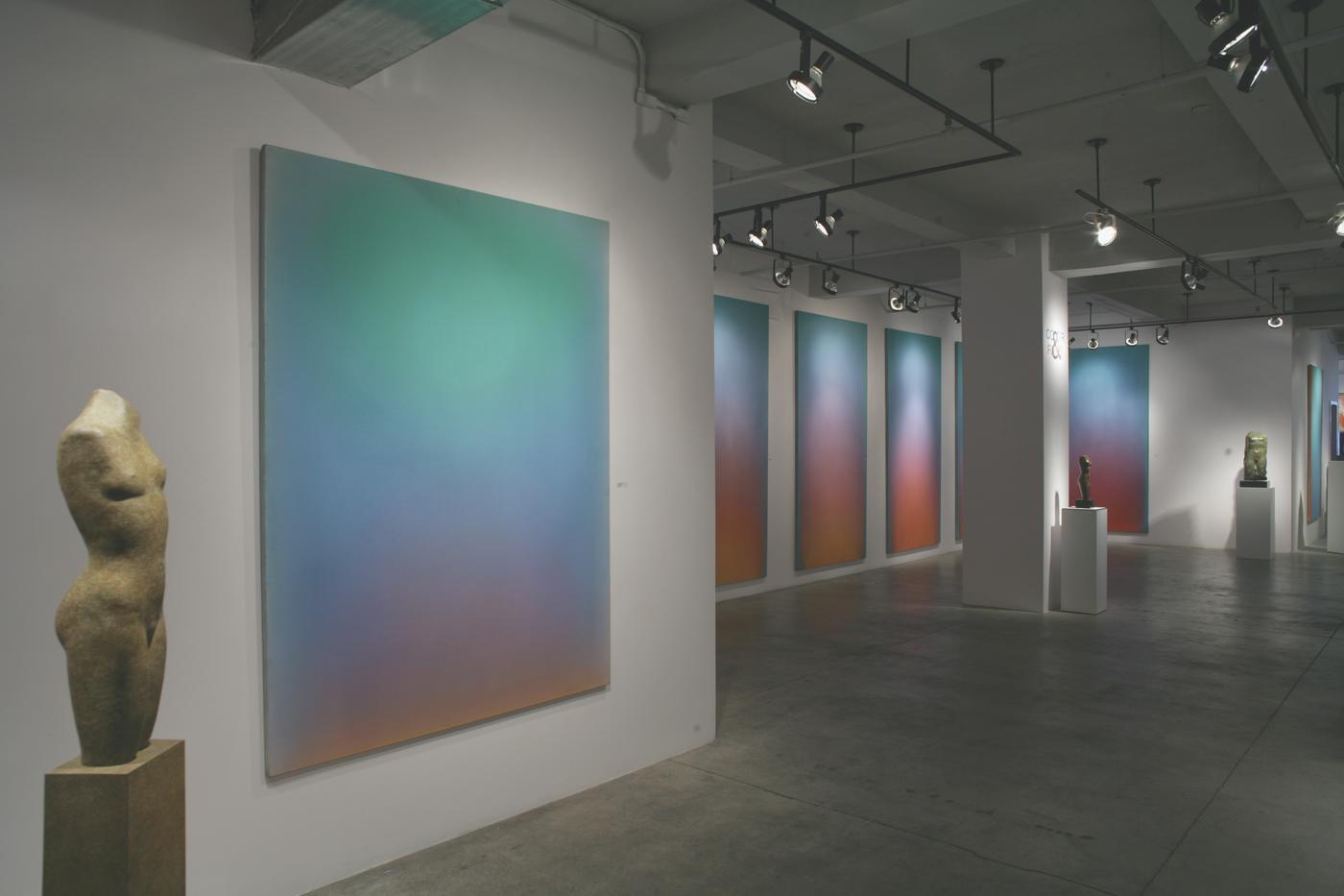 Installation view at ACA Galleries: a large colour-field canvas shading from green through blue to amber, with a stone torso on a plinth and a row of further panels beyond.